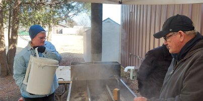 20250313_151259 Jan pouring maple tree sap into the boiler used to make maple syrup. Bruce Whitmore (on the right) is in charge of the boiling operation.